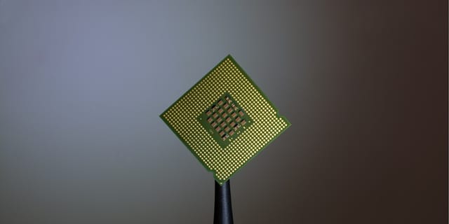 A computer processor held by black tweezers against a neutral background