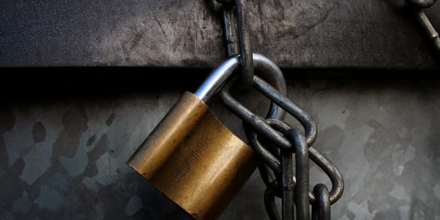 A brass padlock hanging from a heavy grey metal chain.