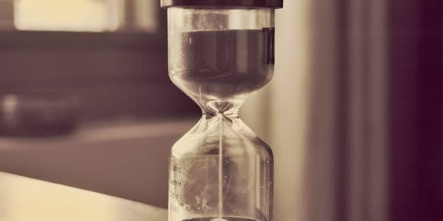 An hourglass counting down on a desk, sand falling through the narrow neck