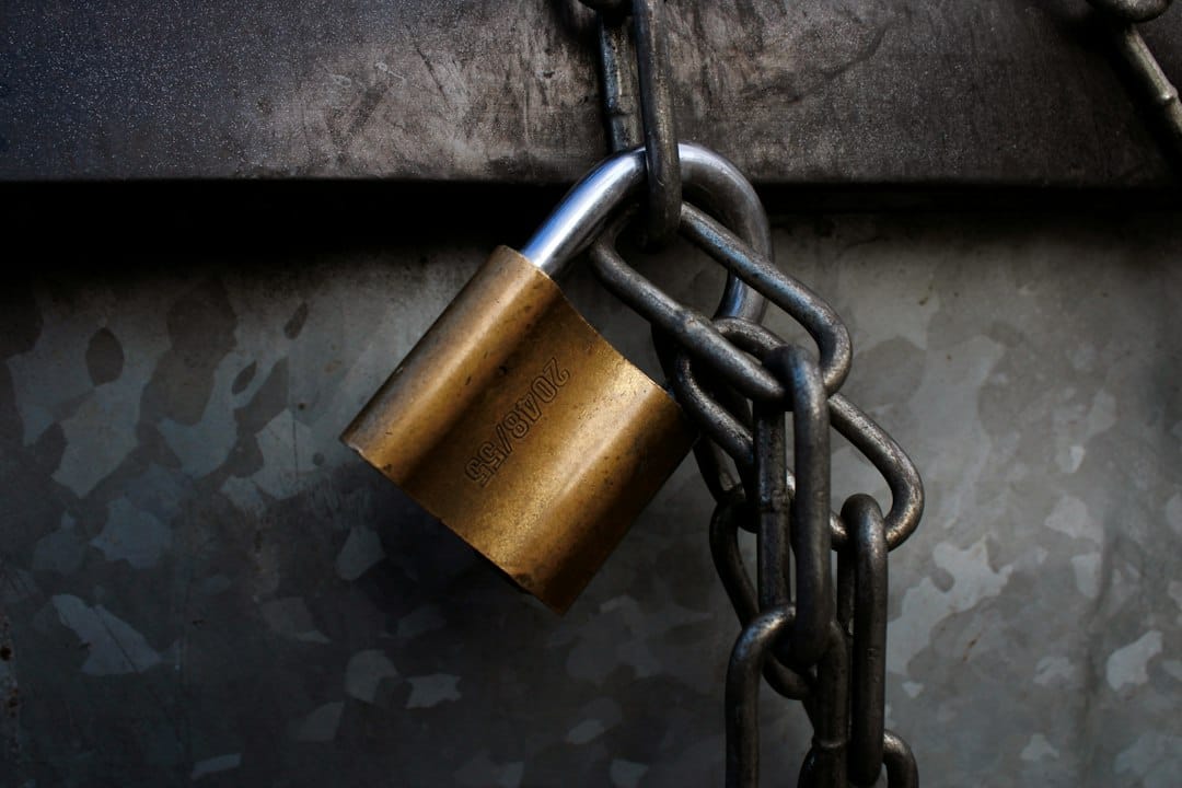 A brass padlock hanging from a heavy grey metal chain.