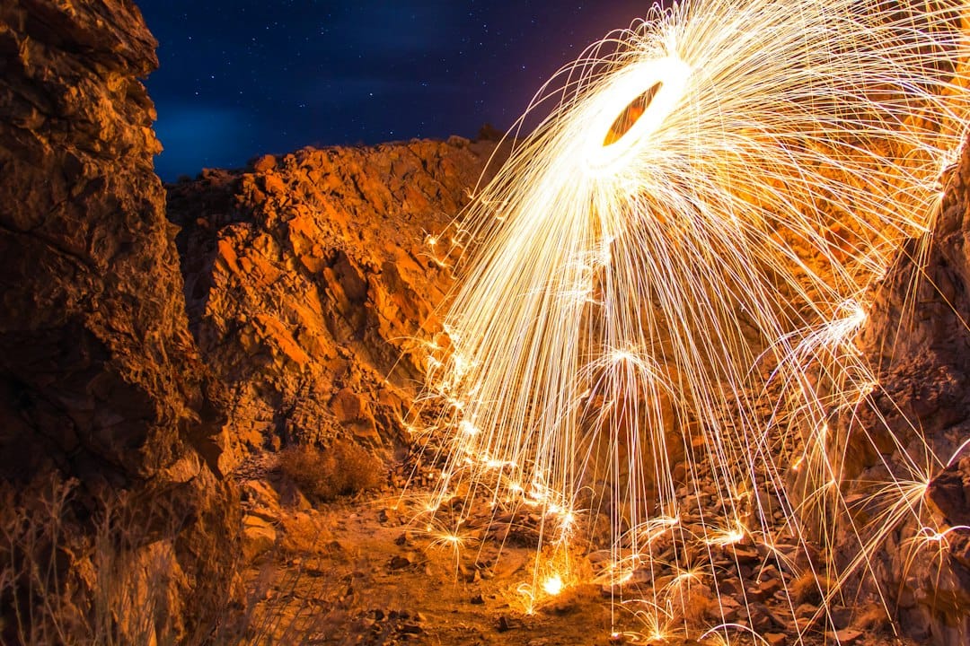 Long-exposure steel wool photography showing glowing sparks and streaks of orange light against a dark background.
