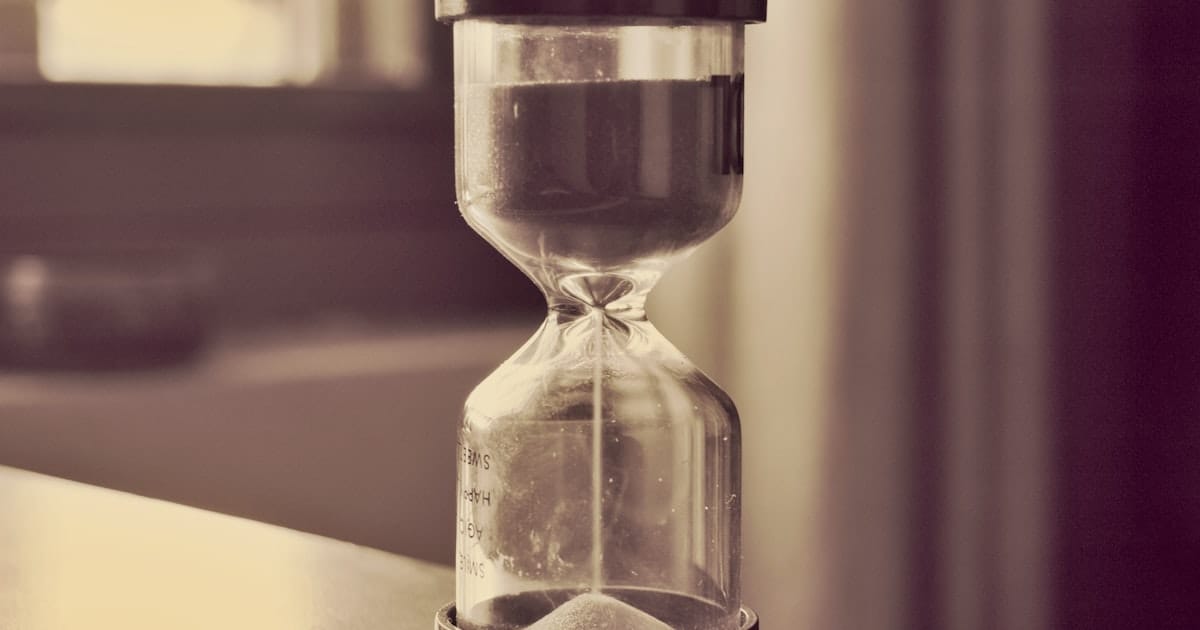 An hourglass counting down on a desk, sand falling through the narrow neck